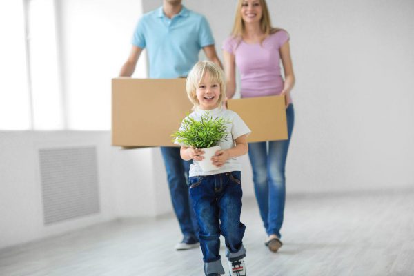 Child happily carrying a plant while parents walk behind with boxes