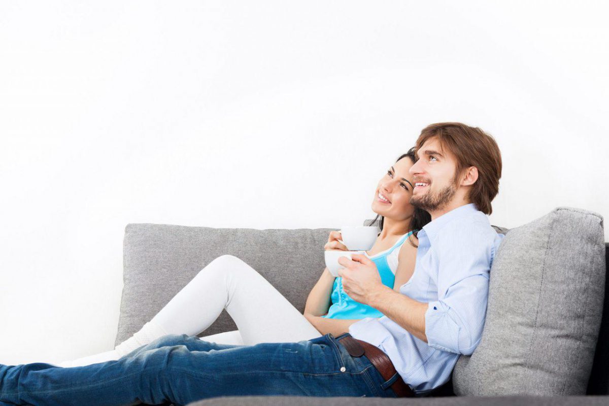 Couple sat drinking coffee on a sofa smiling