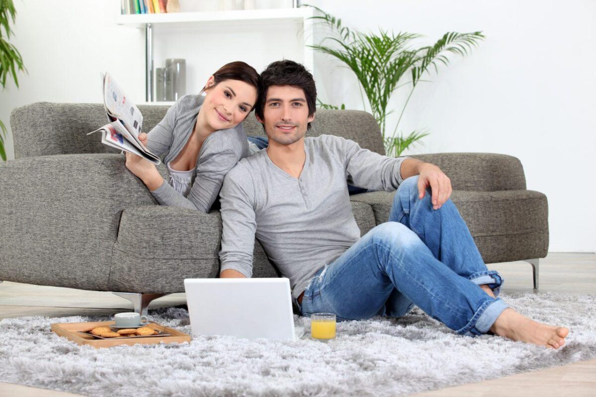 A couple in their living room with laptop smiling at the camera