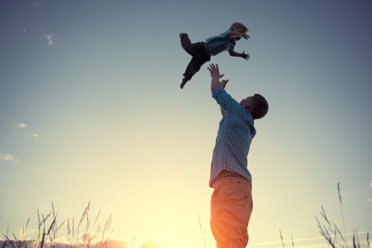 Person throwing child into the air in front of a sunset